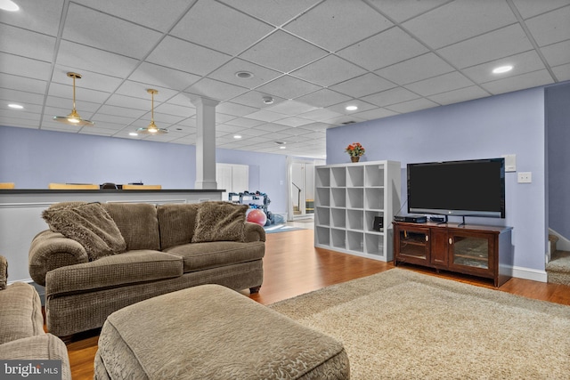 living room with stairs, wood finished floors, baseboards, and a paneled ceiling