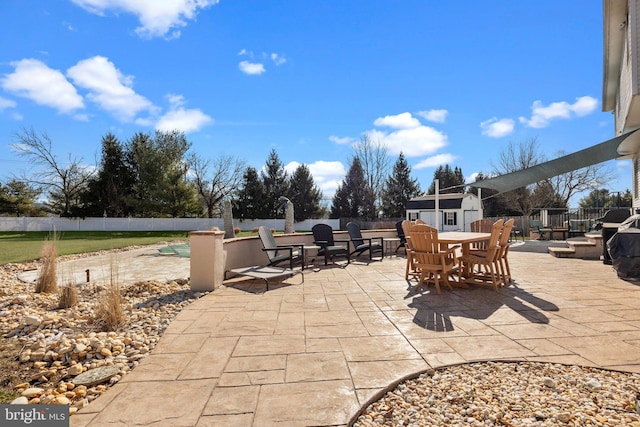 view of patio / terrace with fence, an outbuilding, outdoor dining space, and a shed