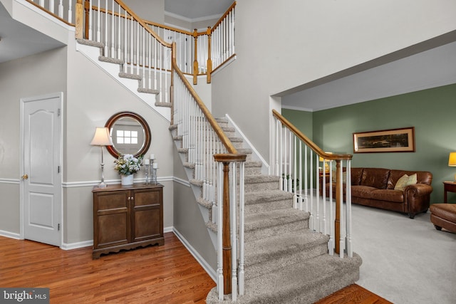 stairway with crown molding, wood finished floors, baseboards, and a towering ceiling