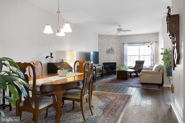 dining room featuring a stone fireplace, ceiling fan with notable chandelier, baseboards, and wood-type flooring