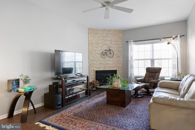 living area featuring a stone fireplace, ceiling fan, baseboards, and wood finished floors