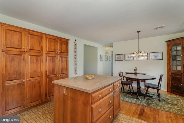 kitchen with visible vents, a kitchen island, pendant lighting, brown cabinets, and a notable chandelier