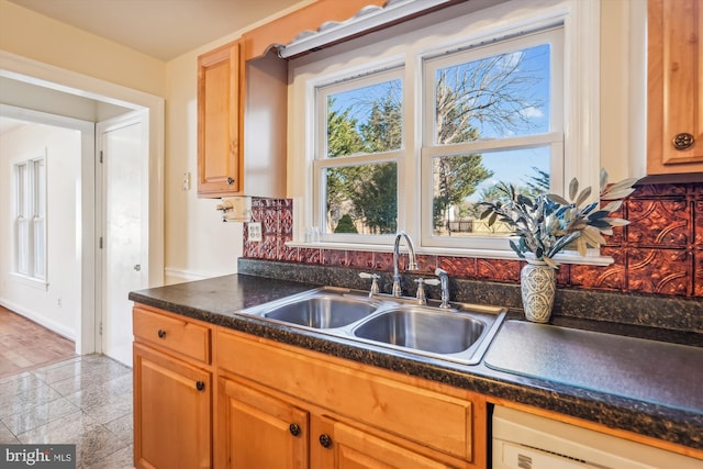 kitchen featuring dishwashing machine, dark countertops, and a sink