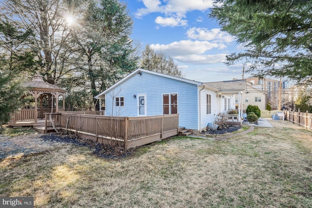 rear view of property featuring a gazebo, a wooden deck, a yard, and fence