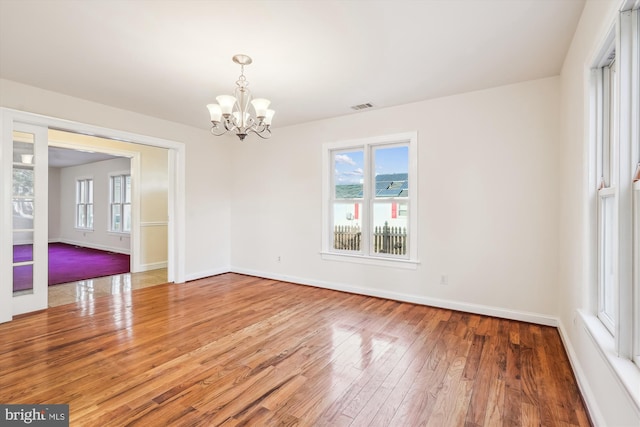 spare room with hardwood / wood-style floors, an inviting chandelier, baseboards, and visible vents