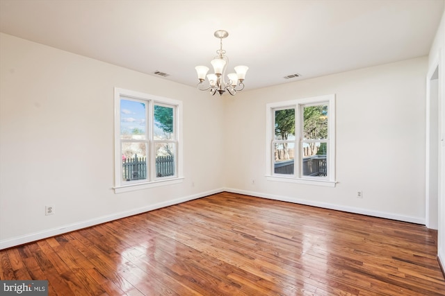 empty room with visible vents, baseboards, an inviting chandelier, and hardwood / wood-style flooring