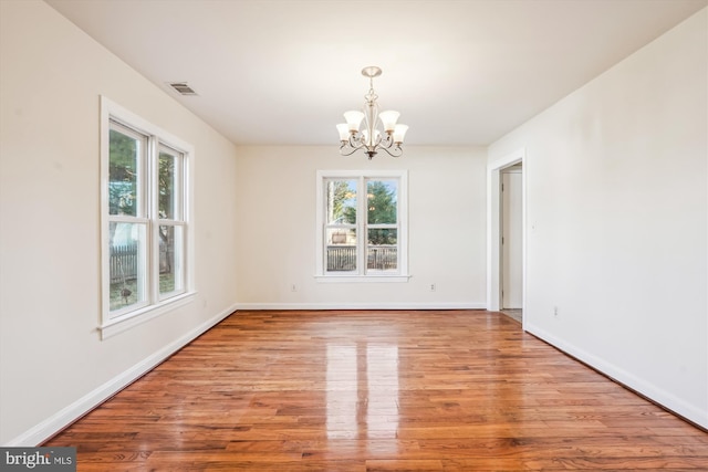 empty room featuring visible vents, baseboards, an inviting chandelier, and wood finished floors