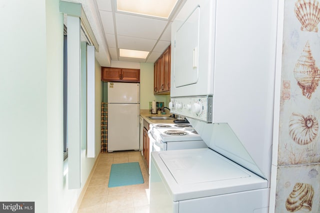 kitchen with white appliances, a drop ceiling, light countertops, stacked washer / dryer, and brown cabinets