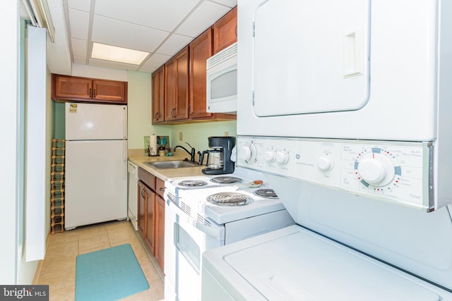 kitchen with brown cabinetry, stacked washer / dryer, white appliances, and a sink