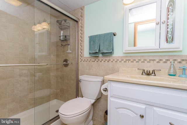 bathroom with a wainscoted wall, toilet, tile walls, a shower stall, and vanity