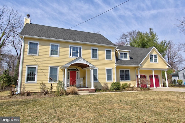 colonial home featuring a shingled roof, a front yard, a chimney, a garage, and driveway