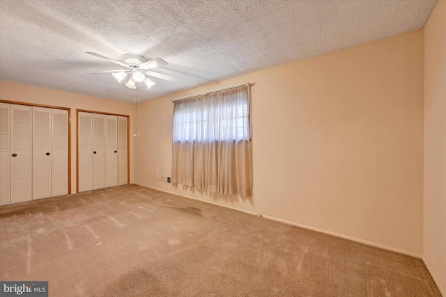 unfurnished bedroom featuring multiple closets, a textured ceiling, carpet floors, and a ceiling fan