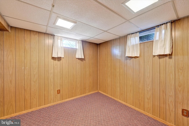 basement with a drop ceiling, baseboards, carpet, and wood walls