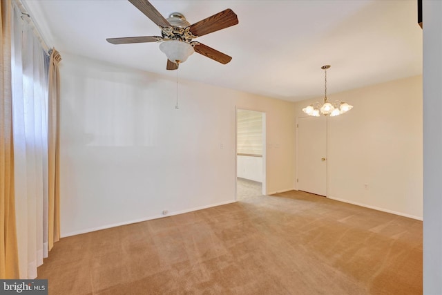 spare room featuring ceiling fan with notable chandelier, baseboards, and light carpet