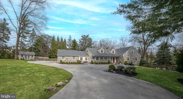 view of front facade featuring aphalt driveway, an outdoor structure, a front lawn, and stone siding