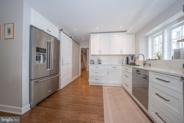 kitchen featuring light wood finished floors, a sink, stainless steel appliances, white cabinetry, and a barn door