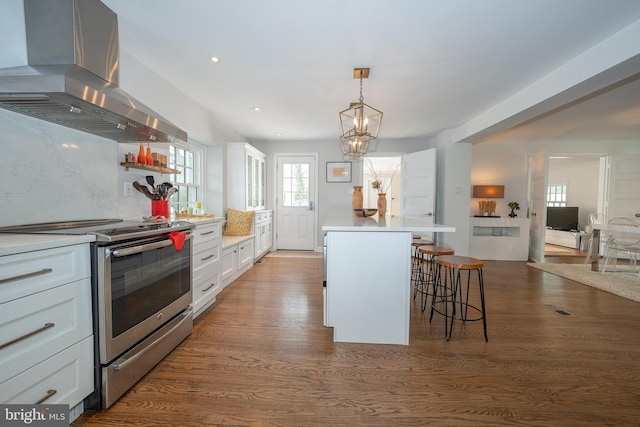 kitchen with a kitchen breakfast bar, stainless steel electric range oven, wall chimney exhaust hood, and dark wood-type flooring