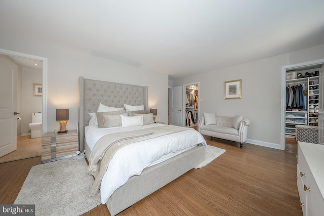 bedroom with a walk in closet, baseboards, a closet, and wood finished floors