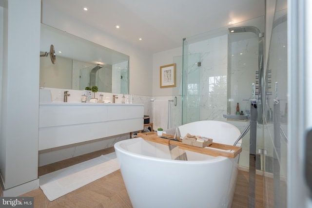 bathroom with a marble finish shower, a soaking tub, double vanity, a sink, and tile walls