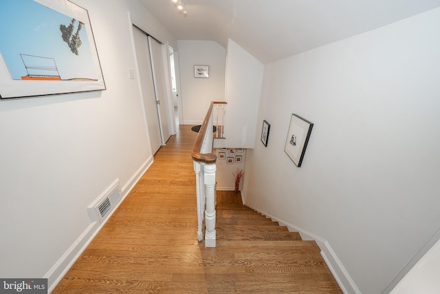 hall featuring visible vents, lofted ceiling, baseboards, and light wood-style flooring