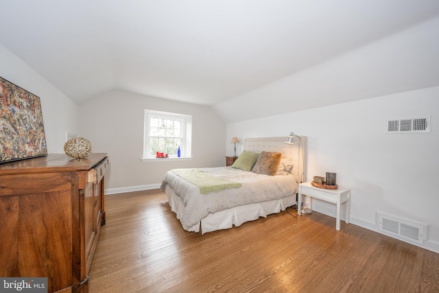 bedroom featuring visible vents, light wood-type flooring, baseboards, and vaulted ceiling