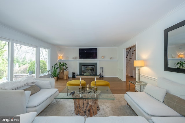 living room with a fireplace with raised hearth, baseboards, stairway, ornamental molding, and wood finished floors