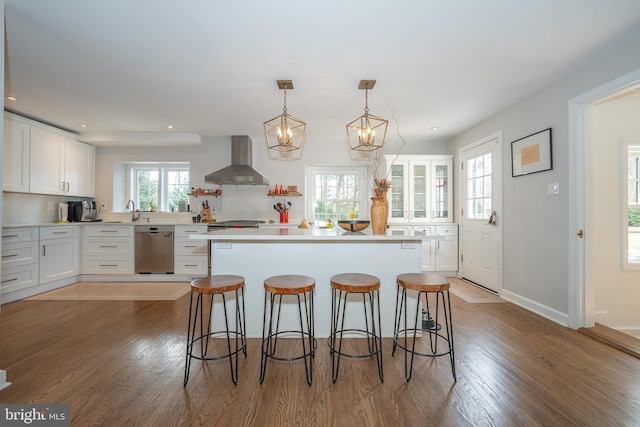 kitchen featuring dishwasher, a kitchen breakfast bar, wall chimney range hood, and white cabinetry