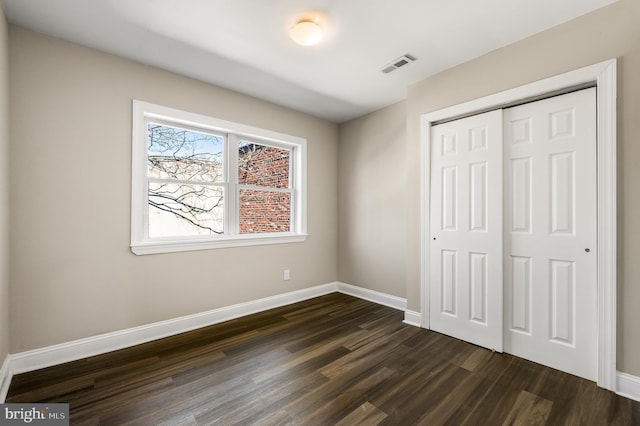 unfurnished bedroom featuring visible vents, baseboards, a closet, and dark wood finished floors