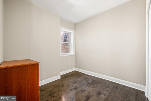 spare room with baseboards and dark wood-style floors