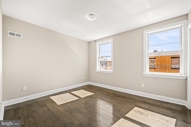 empty room featuring visible vents, baseboards, and dark wood-style floors