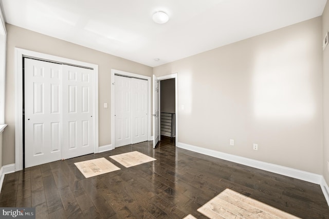 unfurnished bedroom featuring wood finished floors, baseboards, and two closets