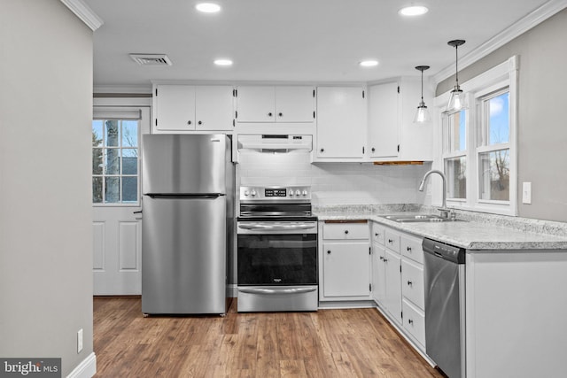 kitchen featuring under cabinet range hood, ornamental molding, appliances with stainless steel finishes, white cabinetry, and a sink