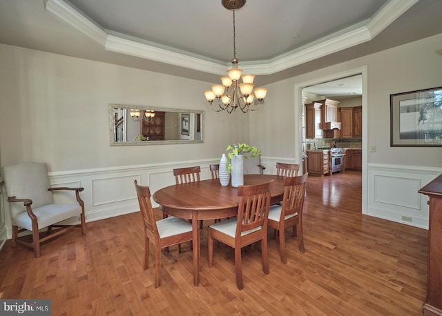 dining area with crown molding, a wainscoted wall, wood finished floors, a decorative wall, and a raised ceiling