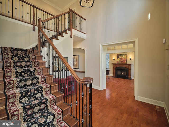 stairway with a fireplace with flush hearth, ornamental molding, baseboards, and wood finished floors