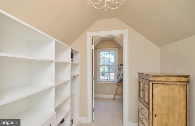 spacious closet featuring lofted ceiling, light colored carpet, and a chandelier