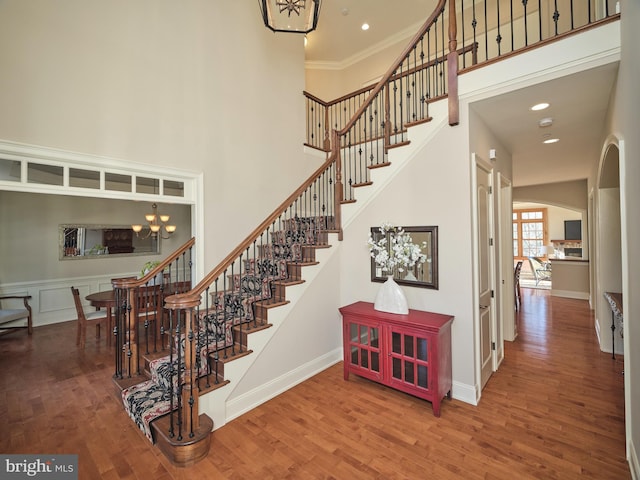 staircase featuring baseboards, arched walkways, wood finished floors, and a towering ceiling