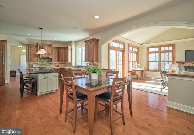 dining area featuring recessed lighting, arched walkways, a stone fireplace, light wood finished floors, and baseboards