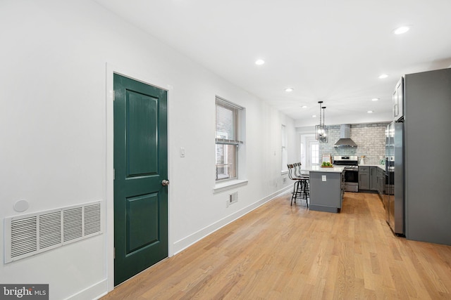 kitchen with visible vents, wall chimney range hood, stainless steel appliances, a breakfast bar area, and light wood finished floors