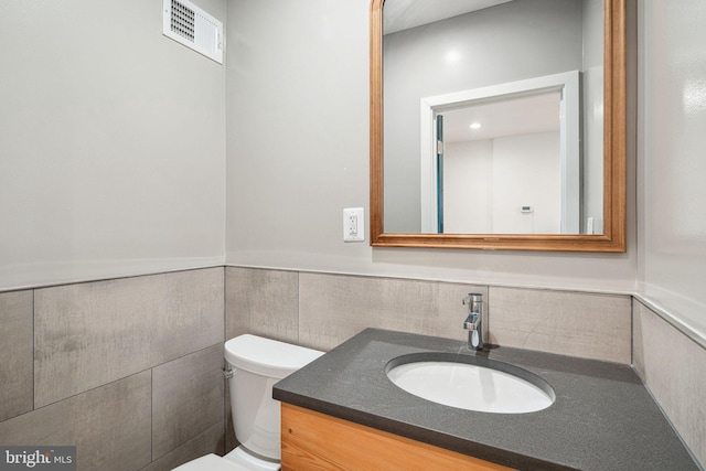 bathroom featuring vanity, a wainscoted wall, visible vents, tile walls, and toilet