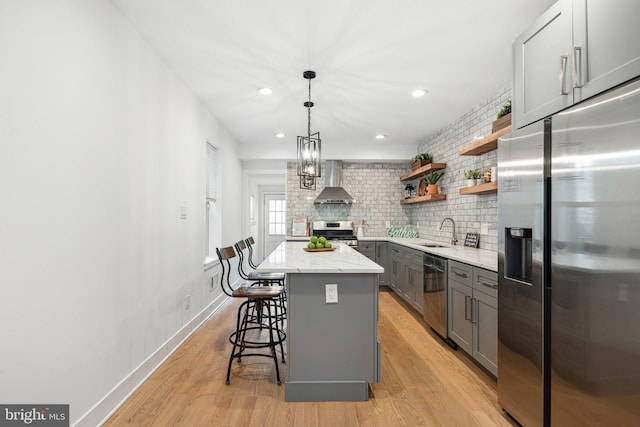 kitchen with light stone counters, open shelves, gray cabinetry, appliances with stainless steel finishes, and wall chimney range hood