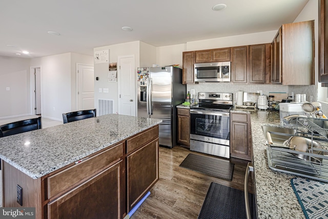 kitchen featuring visible vents, light stone counters, wood finished floors, stainless steel appliances, and decorative backsplash