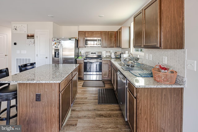 kitchen featuring stainless steel appliances, a kitchen breakfast bar, tasteful backsplash, and wood finished floors