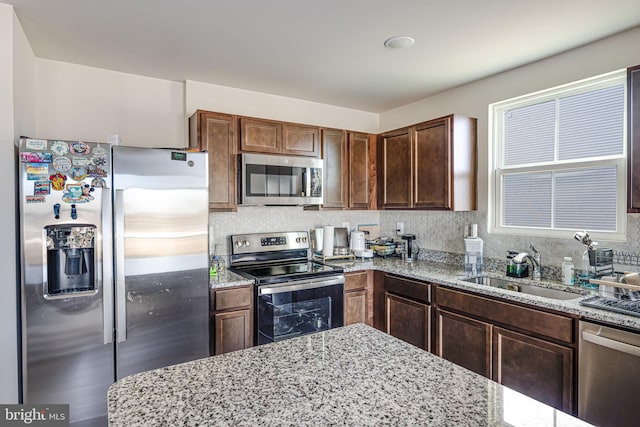 kitchen with decorative backsplash, light stone counters, appliances with stainless steel finishes, and a sink