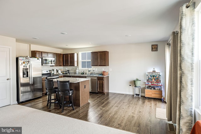 kitchen with dark brown cabinets, appliances with stainless steel finishes, dark wood-style floors, and a center island