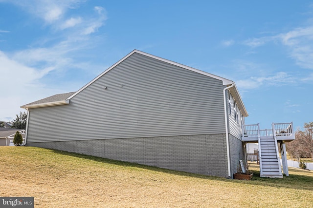 view of side of home with brick siding, a lawn, a wooden deck, and stairs