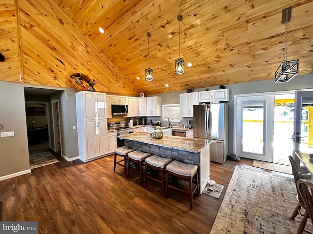 kitchen with a kitchen island, dark wood finished floors, white cabinetry, appliances with stainless steel finishes, and light stone countertops