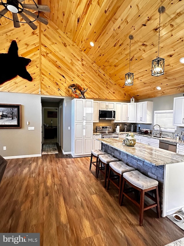 kitchen with light stone counters, dark wood-style floors, stainless steel appliances, white cabinetry, and a kitchen breakfast bar