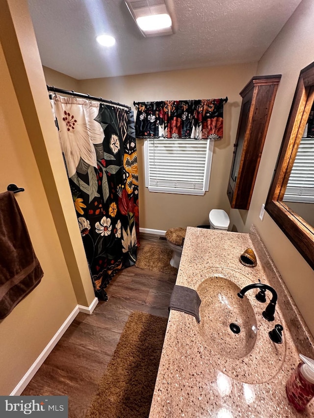 full bathroom featuring toilet, a textured ceiling, wood finished floors, baseboards, and vanity