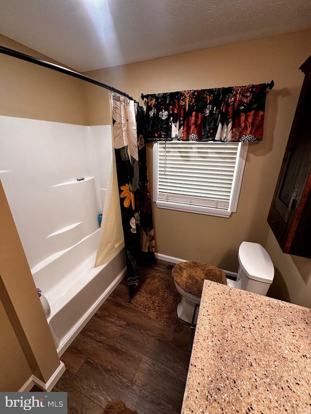 bathroom featuring baseboards, toilet, wood finished floors, shower / bath combination with curtain, and vanity