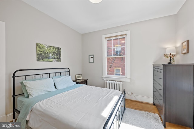 bedroom with radiator heating unit, light wood-style floors, and baseboards